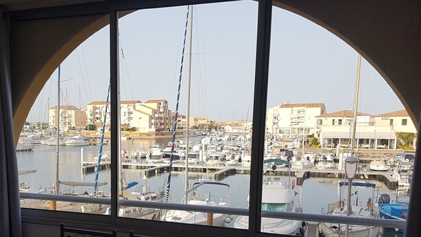 A marina with multiple boats docked, buildings in the background, and a clear sky.