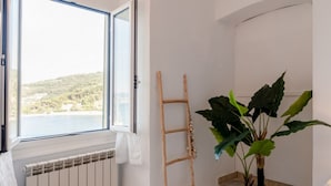 Una habitación con un gran ventanal, un radiador, una escalera de madera y una planta en maceta.