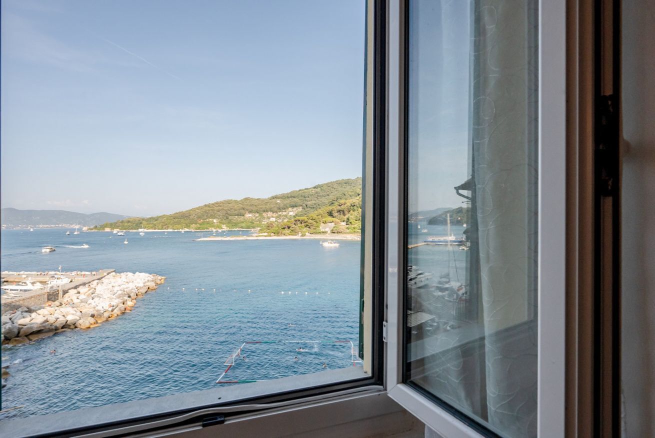 A coastal view through a window with a rocky shoreline, boats, and a distant hill.