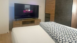 A bedroom with a bed, a TV displaying the Netflix logo, and a wooden wardrobe.