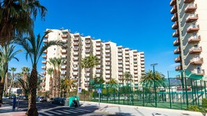 Un edificio residencial de varios pisos con balcones, un paso de peatones y una zona deportiva cercada.
