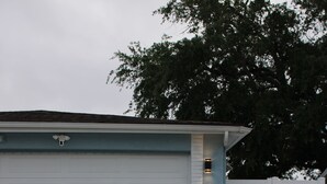 Garagem residencial com calçada de concreto e um pequeno jardim decorativo com cerca de piquete e lanternas.