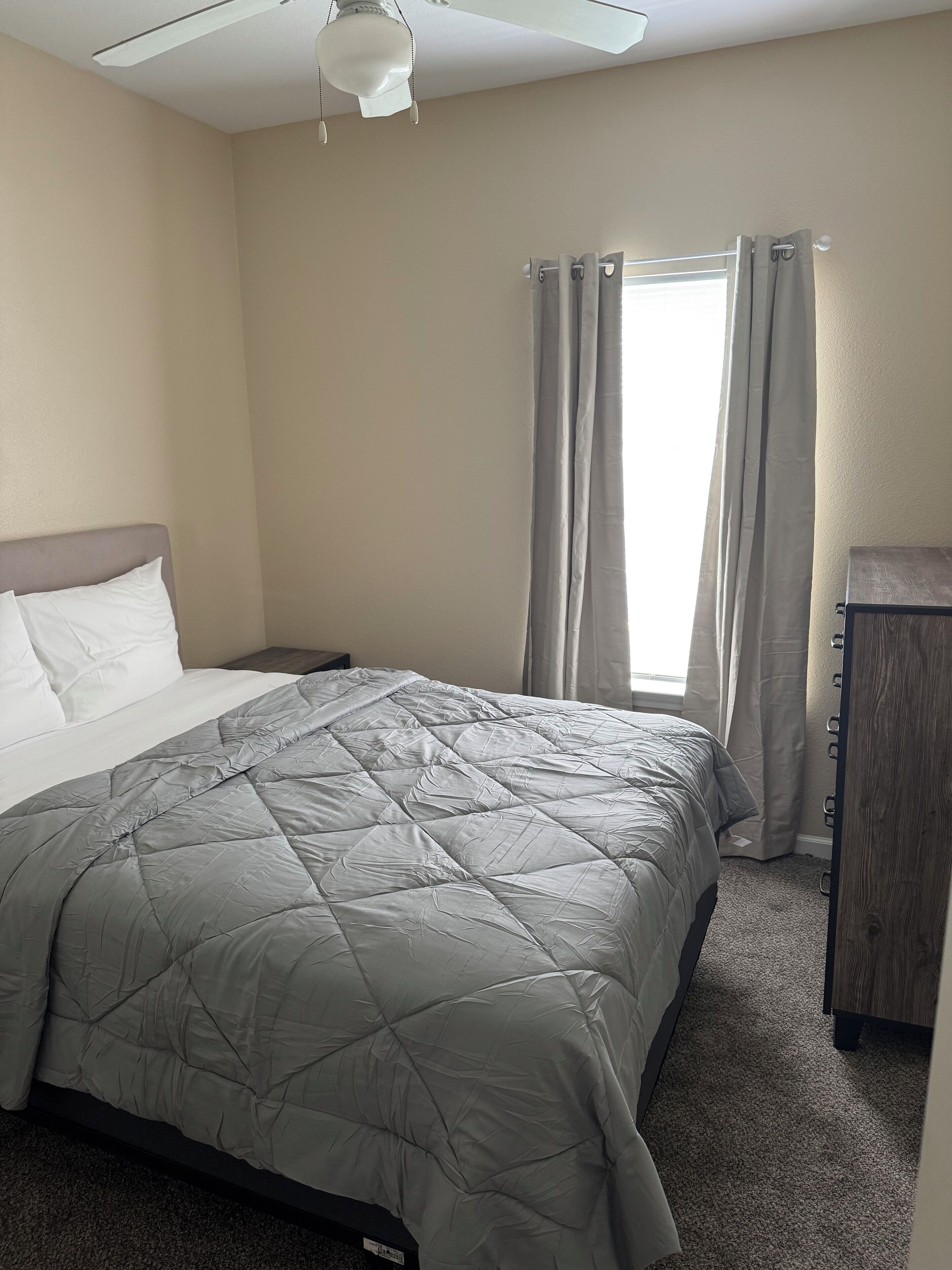A hotel room with a bed, a nightstand, a desk, and a window with curtains.