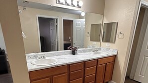 Un baño con lavamanos doble, armarios de madera, encimera de mármol y un espejo grande con iluminación superior.