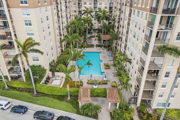 Un immeuble de grande hauteur doté d’une piscine centrale, entourée de palmiers et agrémentée d’espaces de détente en plein air.