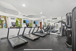 Ein Fitnessstudio mit Laufbändern, Kraftgeräten und einem digitalen Bildschirm.