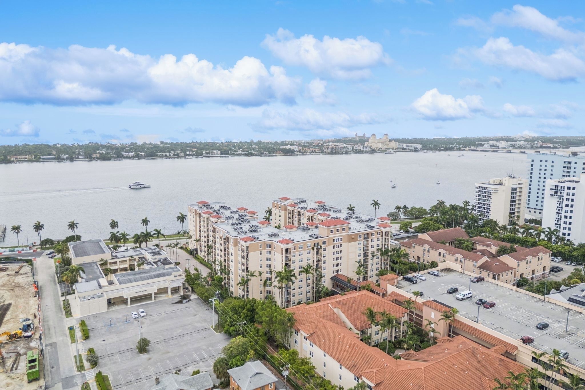 A high-rise hotel with a rooftop pool, a parking lot, and a view of the water body.