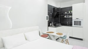 A compact, modern room with a white sofa, a small dining table, and a kitchenette area. - Arion apartment (Athina)