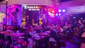 Un restaurante con letrero de neón, mesas, sillas y comensales.