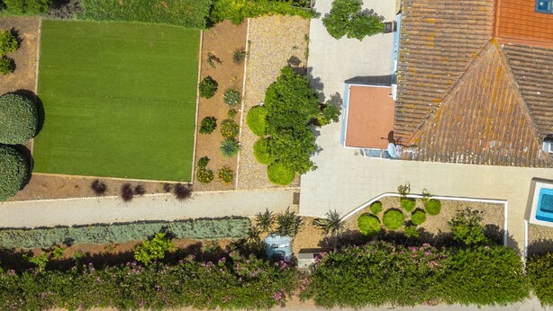 An aerial view of a property with a large lawn, a swimming pool, and a patio area with yellow chairs and umbrellas. - Villa Caicco (Lagos)