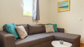 A grey sectional sofa with teal and beige cushions, a small white table with a bowl, and a painting of a beach scene on the wall. - Villa Caicco (Lagos)