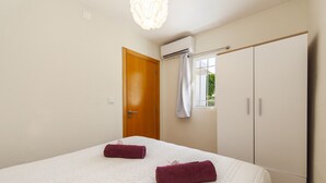 A bedroom with a bed, a wardrobe, an air conditioning unit, and a window with a curtain. - Villa Caicco (Lagos)