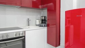 A modern kitchen with red cabinets, a white countertop, and a stainless steel oven. - Estia apartment (Athina)