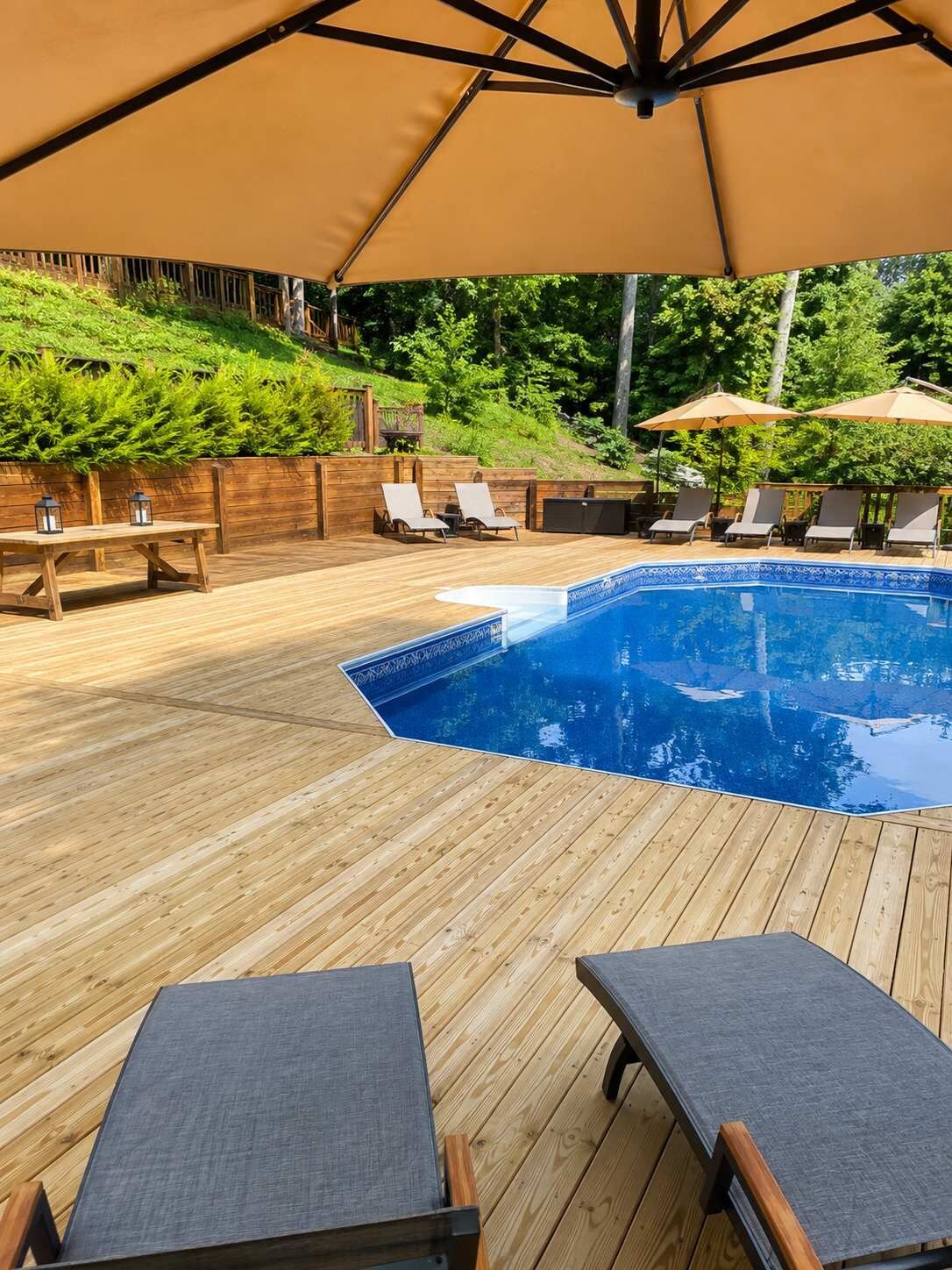 Eine Holzterrasse mit Swimmingpool, Liegestühlen und Sonnenschirmen.