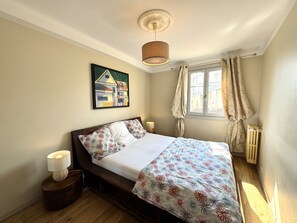 Une chambre à coucher avec un lit, une lampe de chevet, une fenêtre avec des rideaux, un radiateur et un tableau accroché au mur.