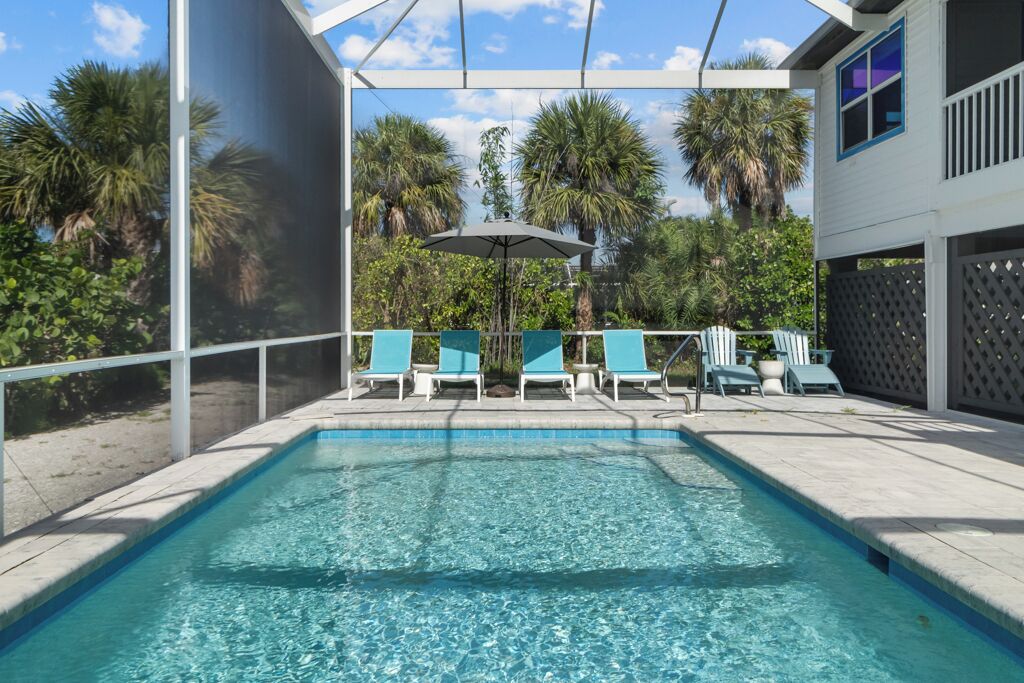 A swimming pool with clear water, surrounded by lounge chairs and a pergola with an umbrella.
