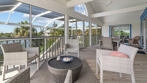 A covered outdoor deck with wicker furniture, a round table, and a view of the ocean.