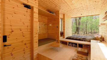 L’intérieur d’un chalet en bois, avec un lit, une petite table et une fenêtre donnant sur une forêt.