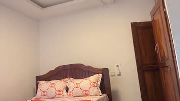 Un dormitorio con una cama de madera, una colcha estampada, un techo blanco con lámpara y un piso a cuadros.