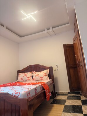 Un dormitorio con una cama de madera, una colcha estampada, un techo blanco con lámpara y un piso a cuadros.
