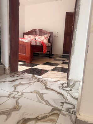 A room with a checkered floor, a bed with a patterned bedspread, and a wooden headboard.