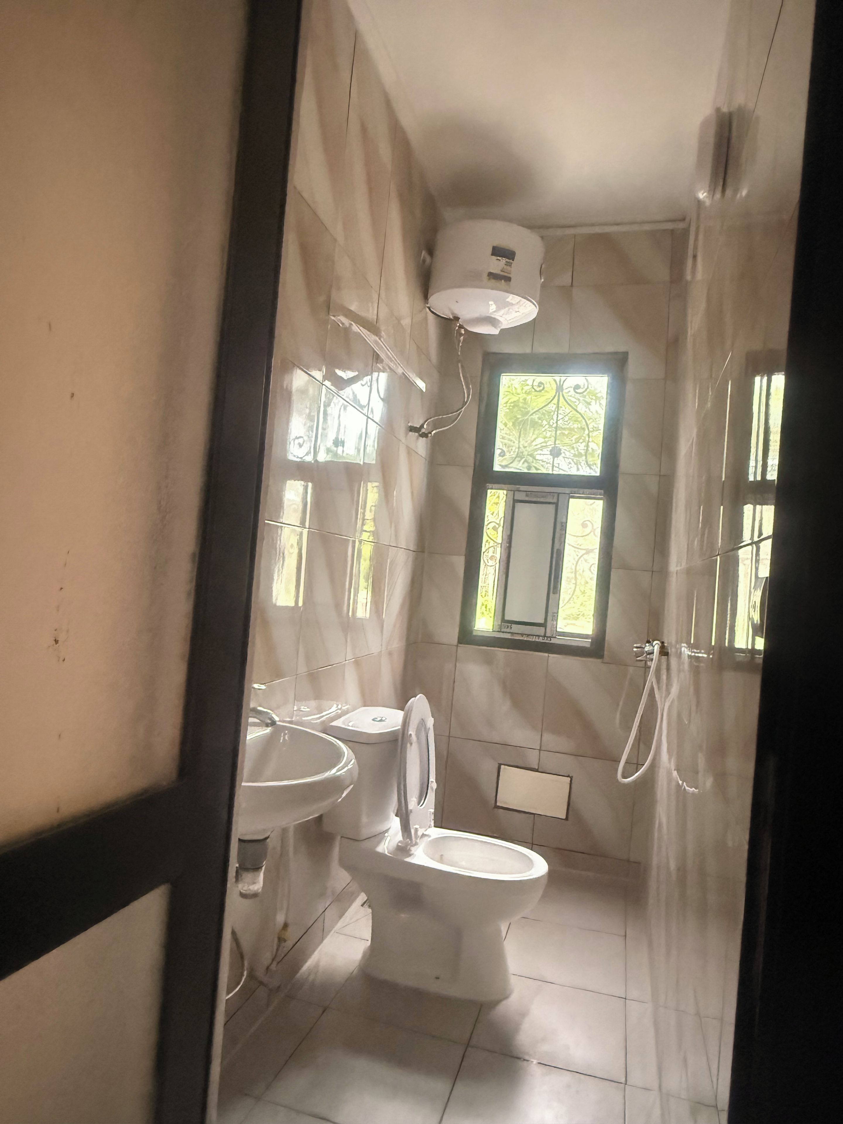 Baño con inodoro, lavamanos y ducha. Hay una ventana que proporciona luz natural.