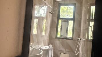 Baño con inodoro, lavamanos y ducha. Hay una ventana que proporciona luz natural.