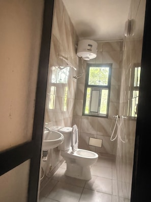 Ein Badezimmer mit Toilette, Waschbecken und Dusche. Ein Fenster sorgt für natürliches Licht.