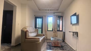 Amplia sala de estar con sofá de cuero, una mesa de centro de vidrio y un televisor de pantalla plana montado en la pared.