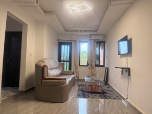 A spacious living room with a leather sofa, a glass coffee table, and a flat-screen TV mounted on the wall.