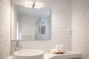 Un baño moderno con un lavamanos blanco, un espejo grande y dos botellas de tocador sobre el mostrador.