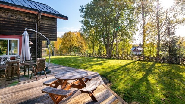 Een houten terras met picknicktafels en stoelen, een overdekte zithoek en uitzicht op een bebost gebied.