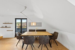 A dining area with a wooden table, four chairs, a pendant light, and a view of the outdoors through a large window. - Spacious Allgäu loft | maisonette style (Nesselwang)