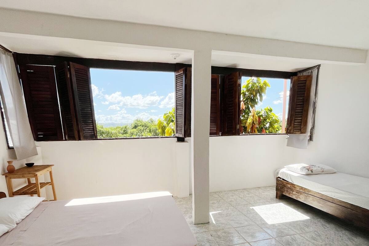 Quarto com cama, uma mesinha e janela com persianas de madeira.