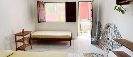 A room with two beds, a wooden table, and a shelf with a plant.