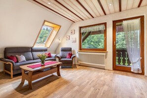 A room with a wooden ceiling, a sofa, a chair, a wooden table, and a window with a view of greenery. - Apartment 'Vogelnest' with Mountain View, Shared Pool and Wi-Fi (Wolfach)