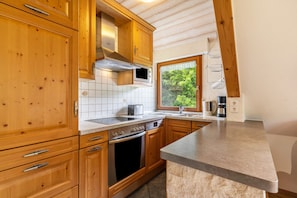 Una cocina con armarios de madera, microondas, horno y ventana con vista a la vegetación.