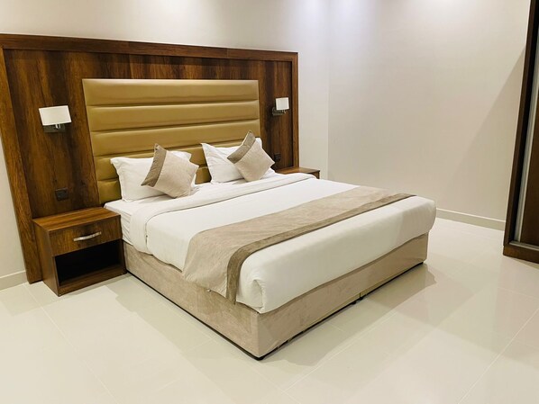 A modern bedroom with a large bed, wooden headboard, bedside tables, and a nightstand with a drawer.