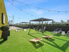 Un espacio exterior bien cuidado con césped artificial, una pérgola y varias sillas de relax.