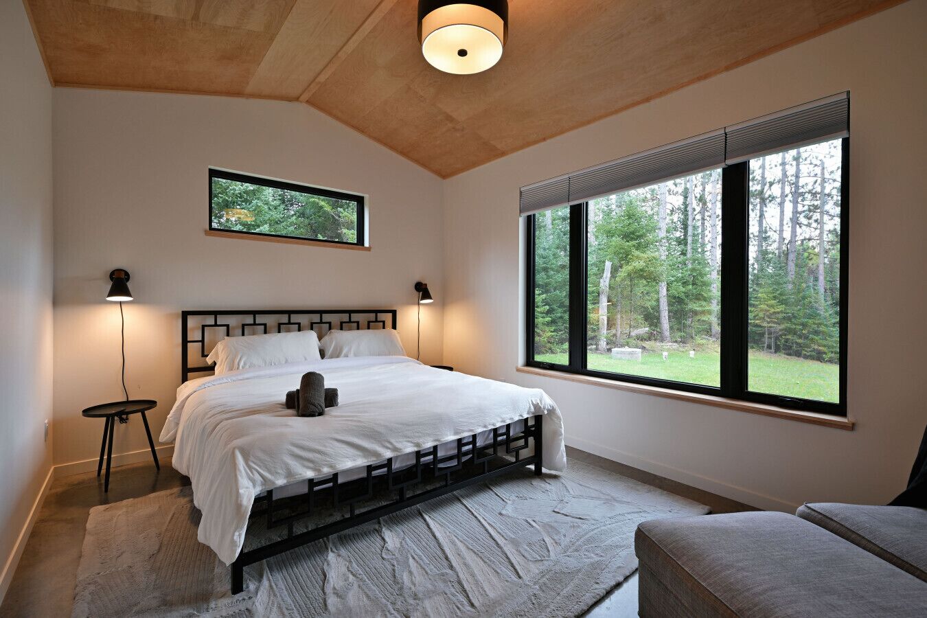 A bedroom with a bed, bedside lamps, a window with a view of trees, and a ceiling light.