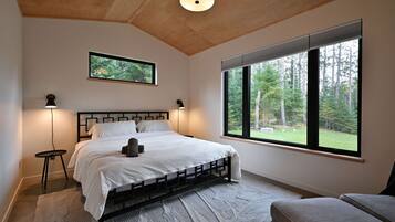 A bedroom with a bed, bedside lamps, a window with a view of trees, and a ceiling light.