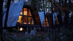 Une série de cabanes aménagées comme des maisons dans les arbres, dotées de grandes fenêtres et d’un foyer central.