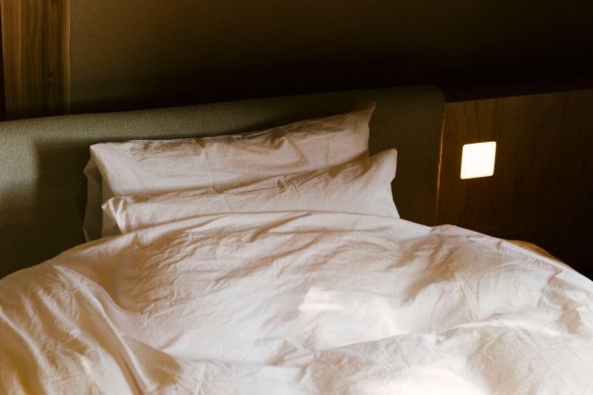A bed with white linens and a headboard.