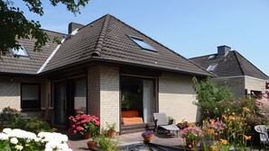A residential house with a sloped roof, a front porch, and a garden with various plants and flowers. - Holiday Apartment 'Ferienwohnung Rathjen' with Private Terrace, Shared Garden and Wi-Fi (Cuxhaven)