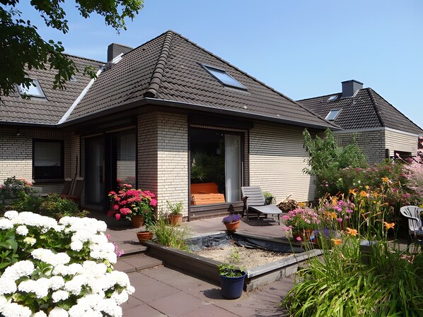 A residential house with a sloped roof, a front porch, and a garden with various plants and flowers.