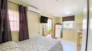 A bedroom with a bed, a TV, and a kitchenette with a fridge and microwave. - Cozy & Central Stay in Curaçao (Willemstad)