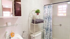 A bathroom with a white sink, toilet, and shower. There is a shelf with a potted plant and folded towels. - Cozy & Central Stay in Curaçao (Willemstad)