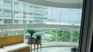 A modern indoor space with a curved bench, potted plants, and a view of a building and greenery through large windows. - CM 304 - luxo conforto em frente ao mar  (Cabo Frio)