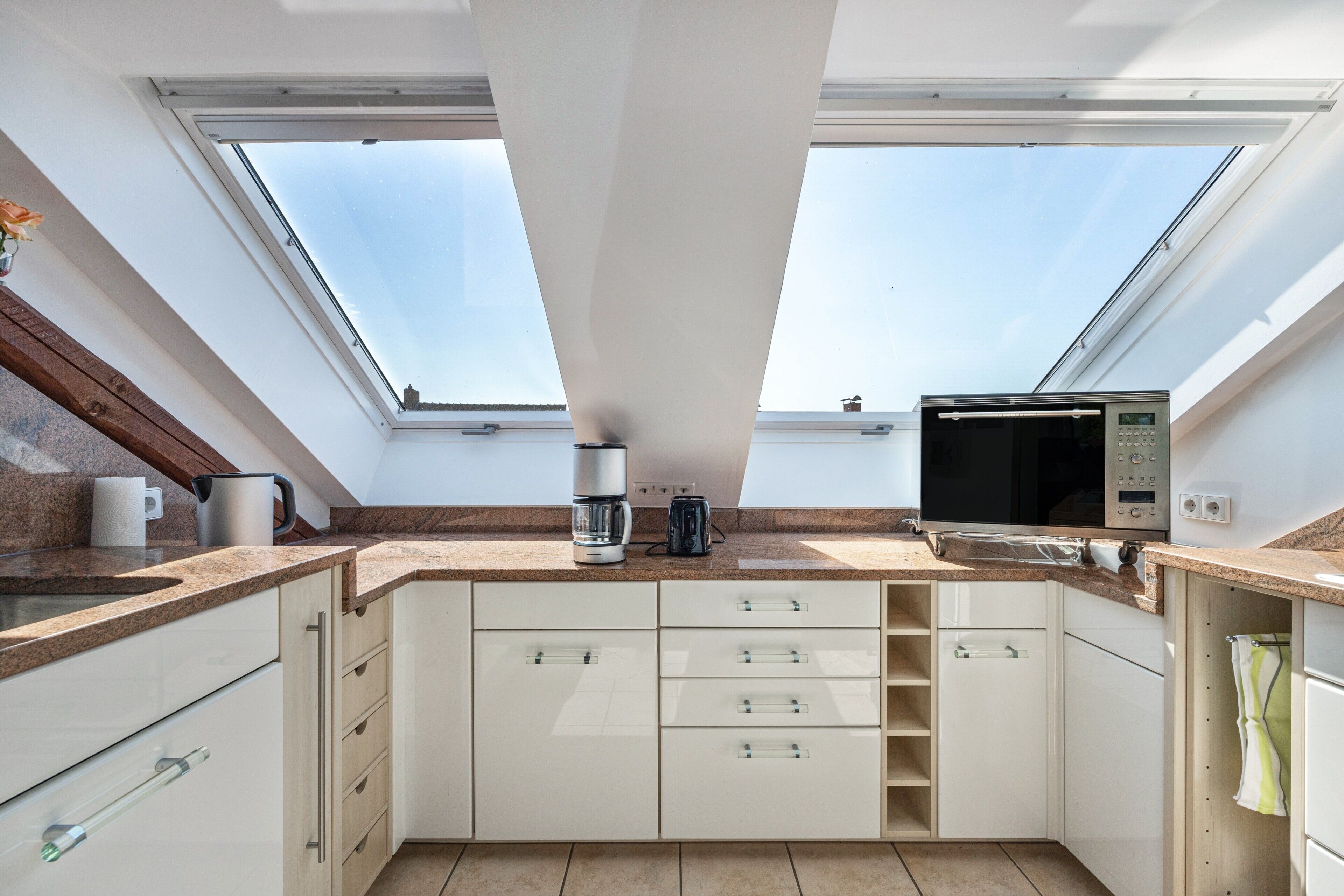 A modern kitchen with skylights, white cabinets, and a microwave.