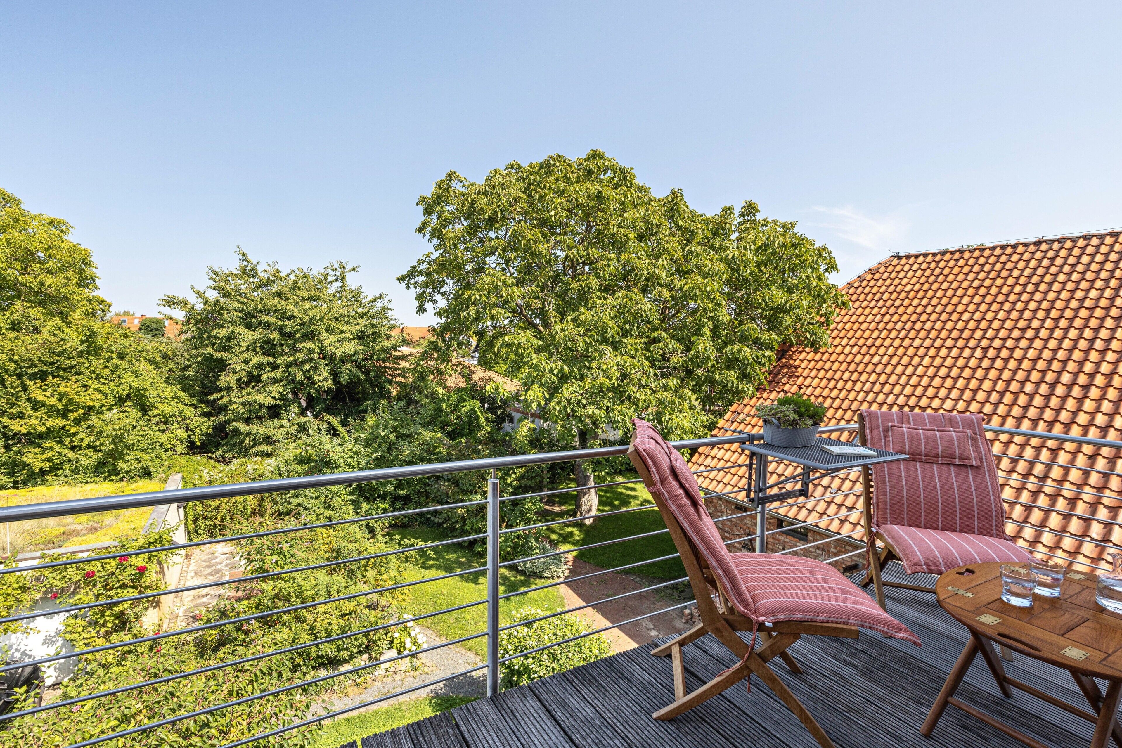 Ein Balkon mit Blick auf einen Garten, ein Tisch mit Stühlen und einem Geländer.